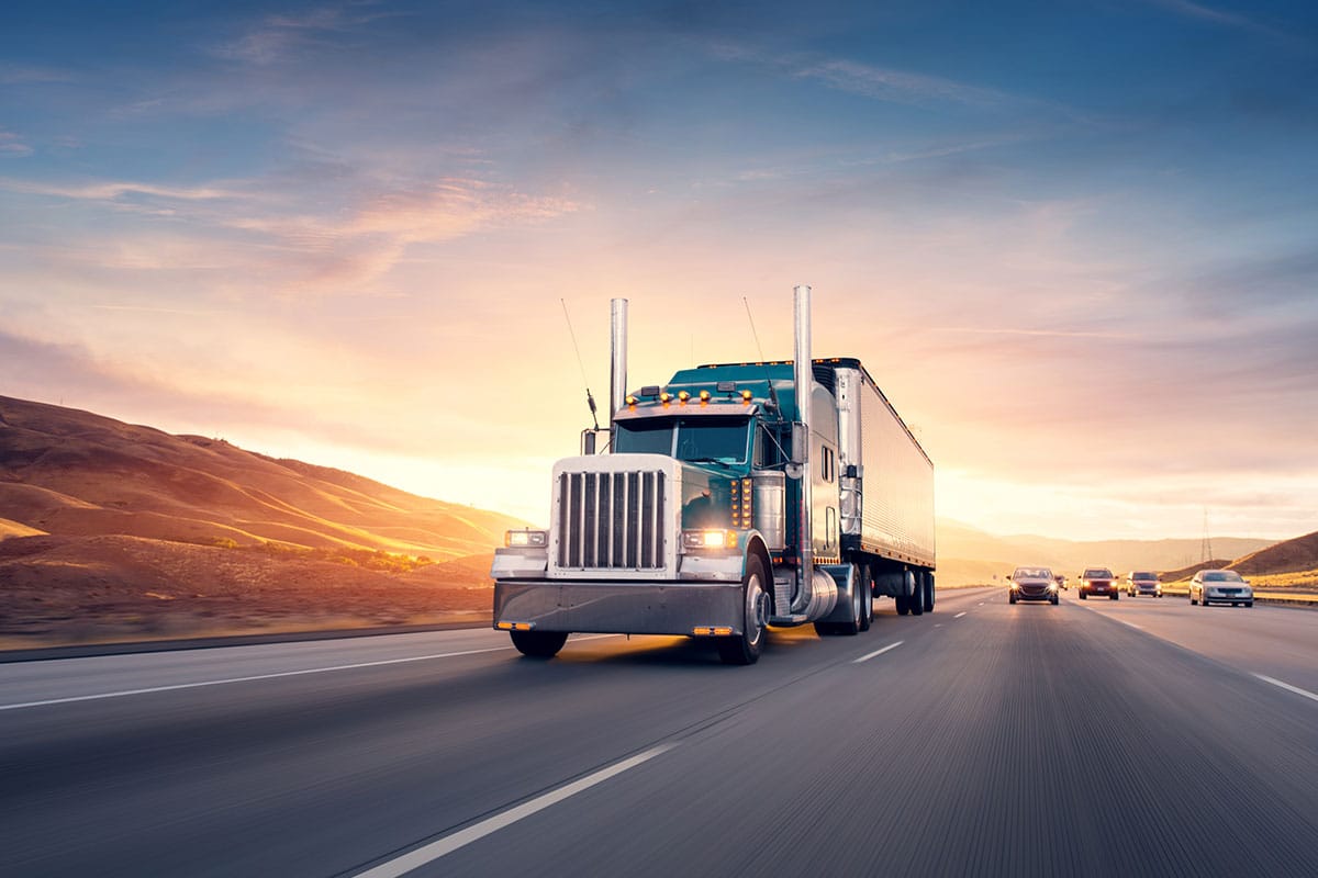 A large commercial semi-truck travelling on an open highway during a scenic sunset.