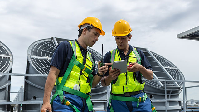 Deux travailleurs de terrain en équipement de sécurité utilisant une tablette dotée du logiciel de gestion de l'effectif mobile de Bell pour coordonner les tâches.
