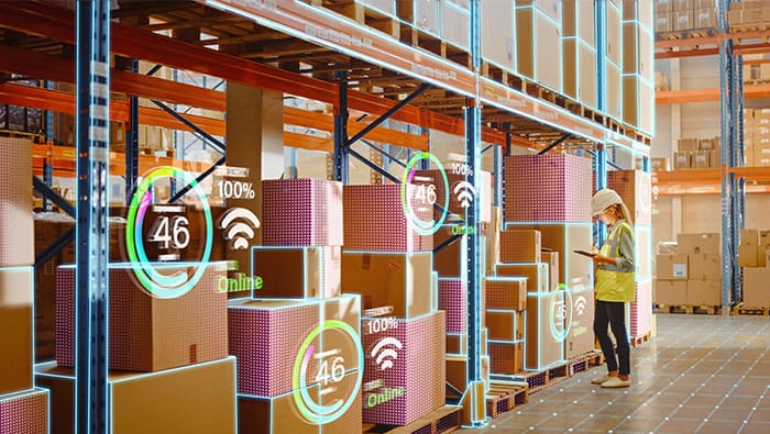 A worker in a warehouse using a tablet to scan and manage inventory, with digital icons showing data being collected from the boxes.