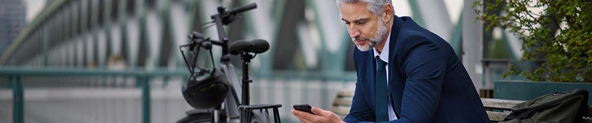 A man sitting next to his bicycle looking at his Snik bike security app on his phone.